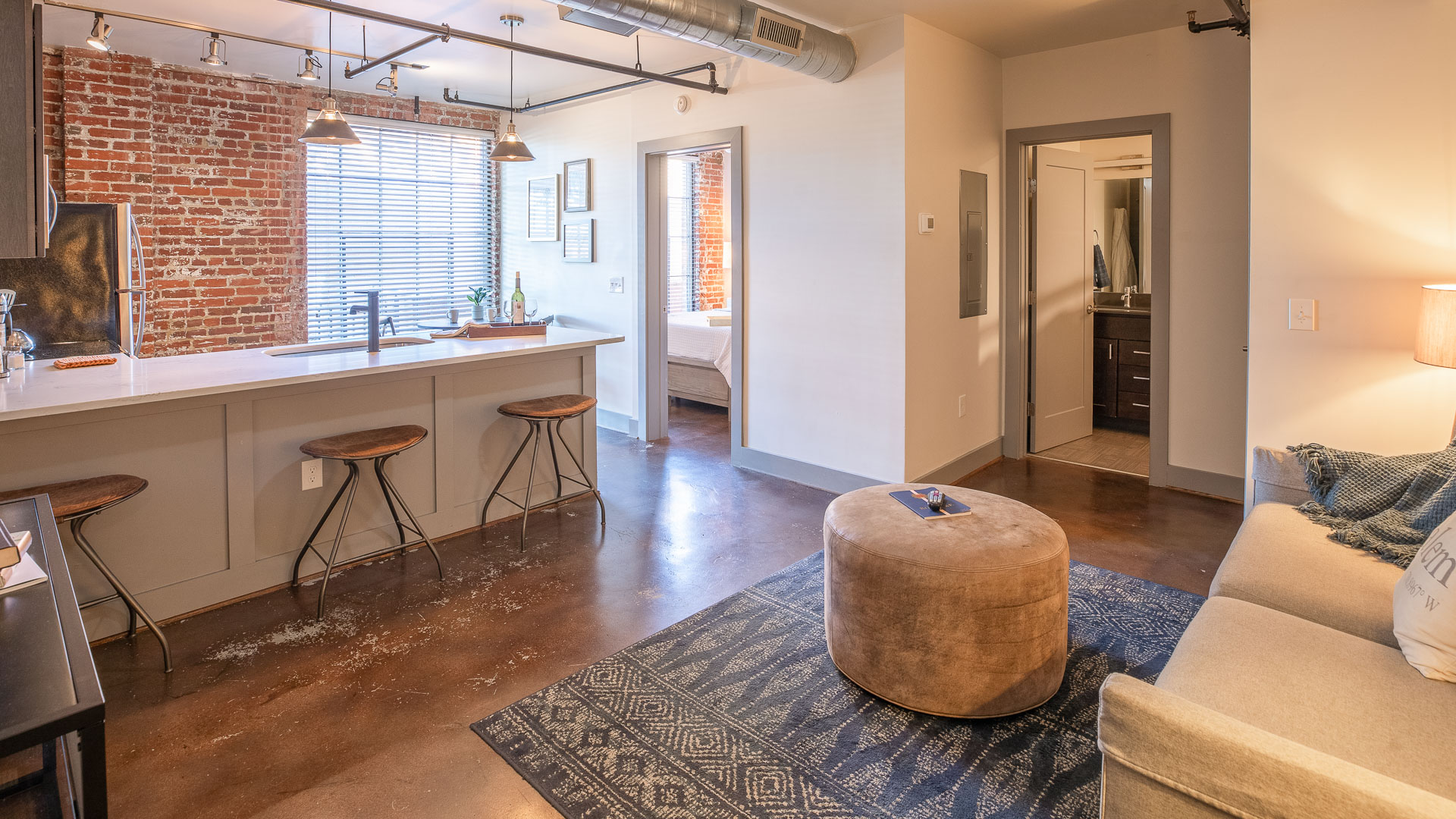 a living room with a stool and a kitchen