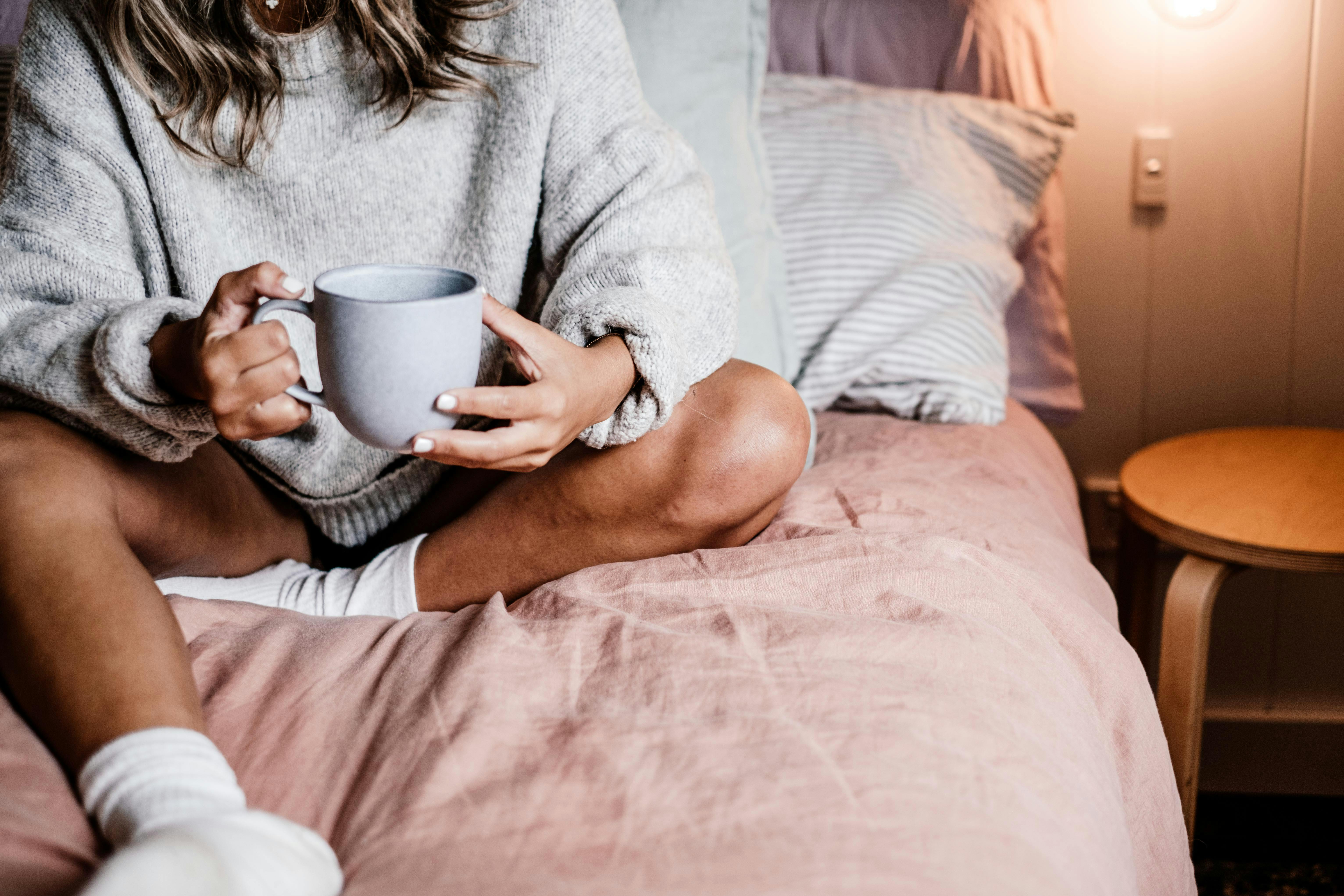 a person sitting on a bed holding a mug