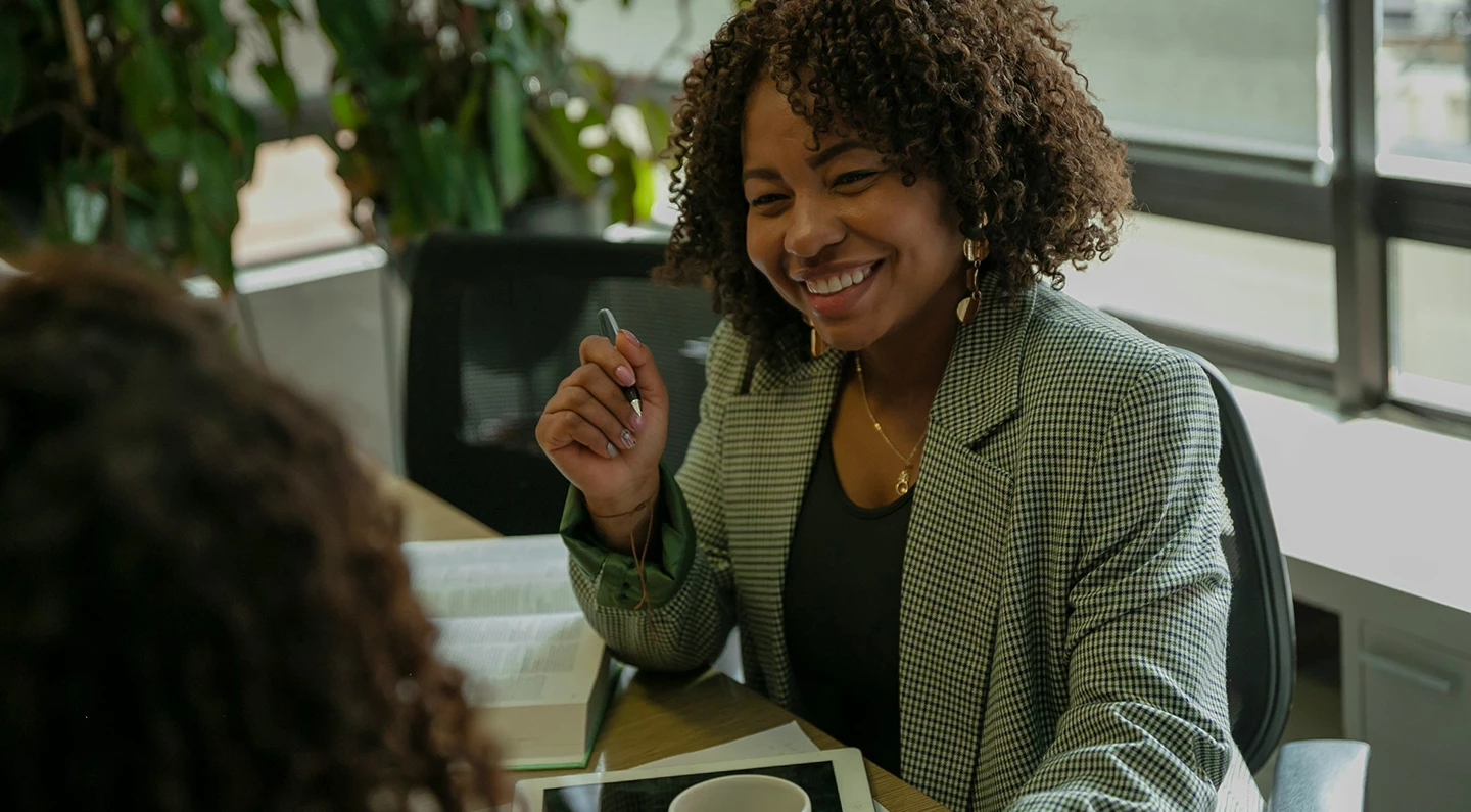 a woman smiling at a table with a book and a pen