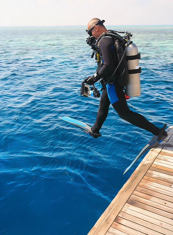 a man in a scuba suit jumping off a dock