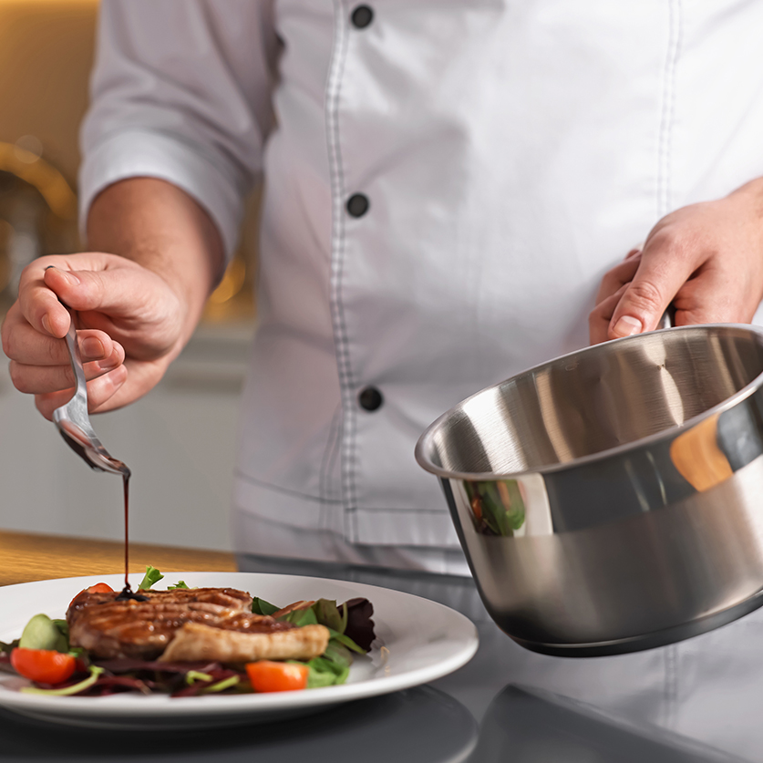 a chef pouring sauce on a plate of food