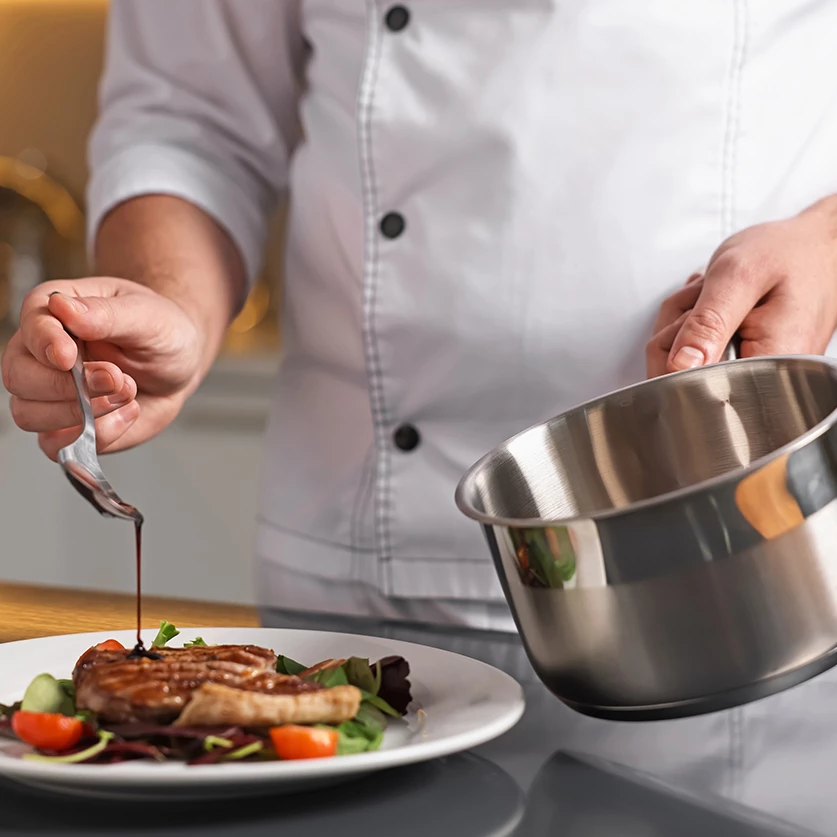 a chef pouring sauce on a plate of food