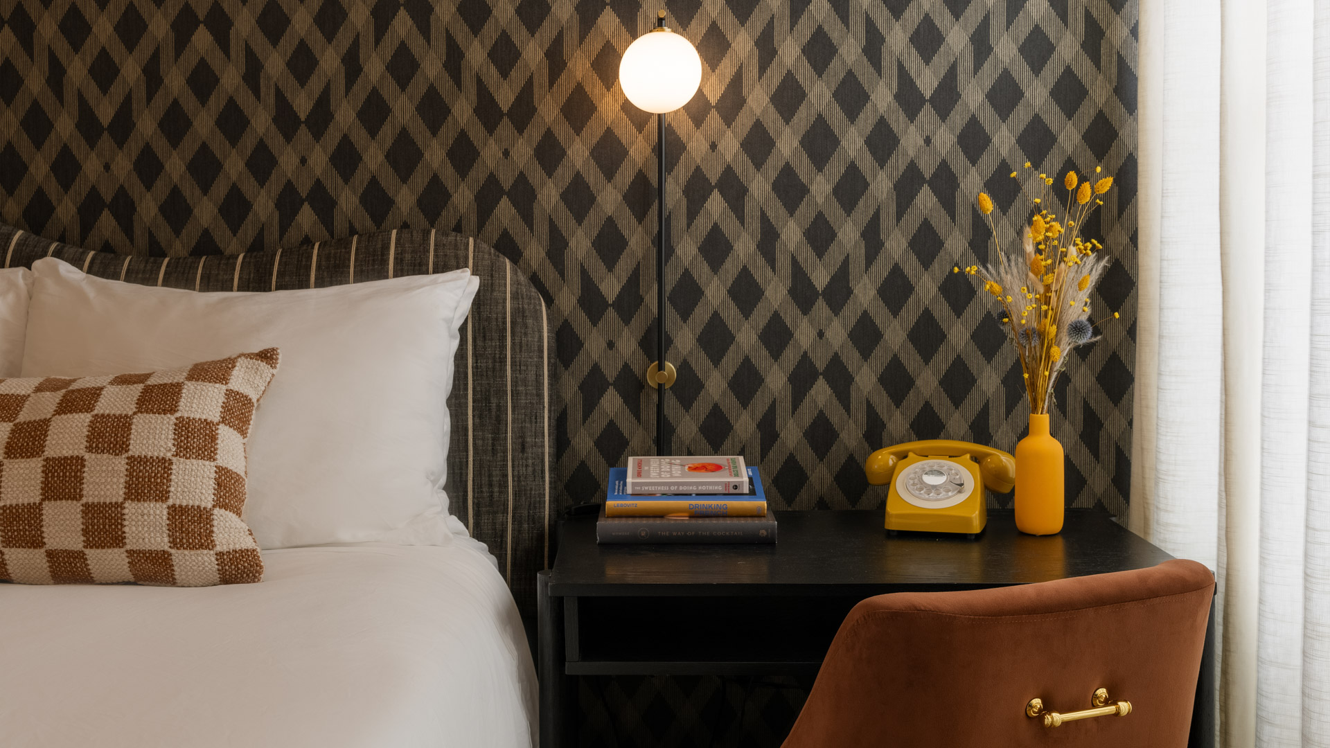 A neatly arranged hotel room with a bed, desk, chair, and lamp.