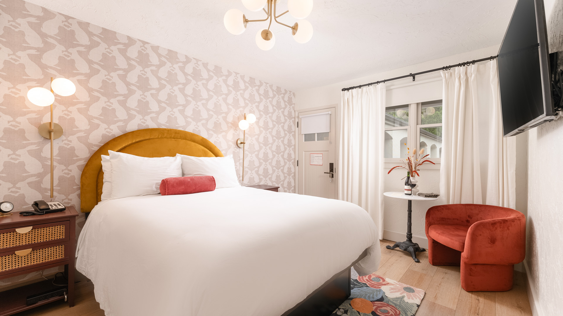 A hotel room with a bed, chair, TV, and window