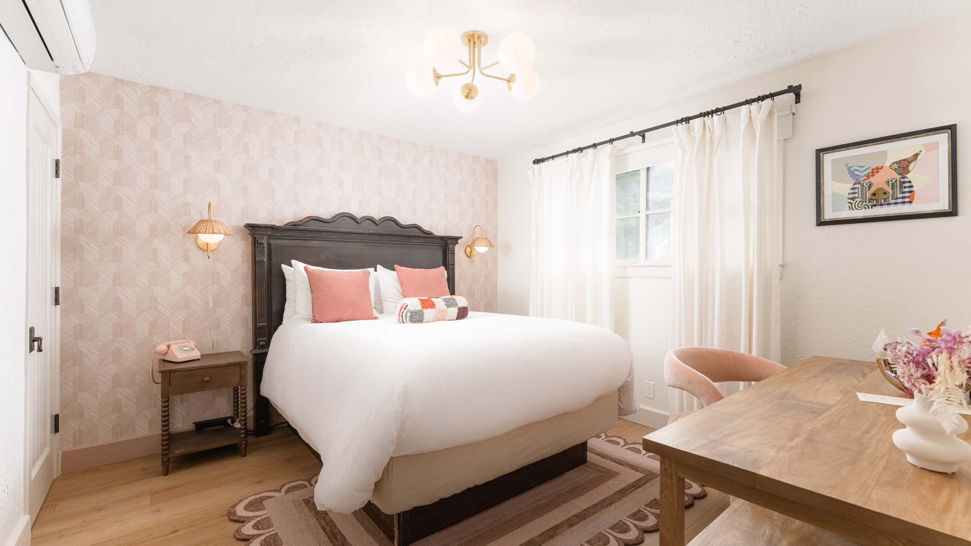A wide view of a guest room with a dark wood bed frame, white bedding, and pink accents.