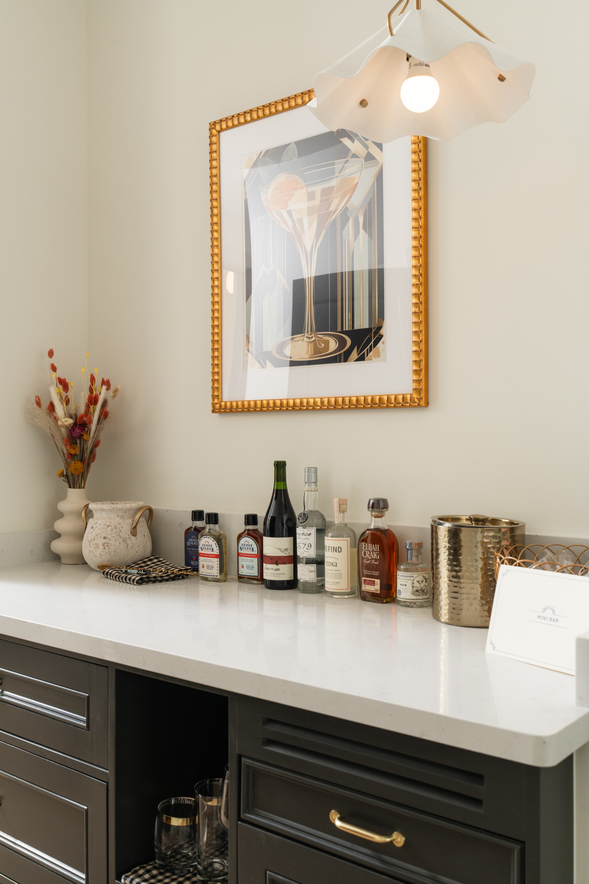 A stylish mini bar with a white marble countertop, dark wood cabinets, and a selection of alcohol bottles and wine glasses.