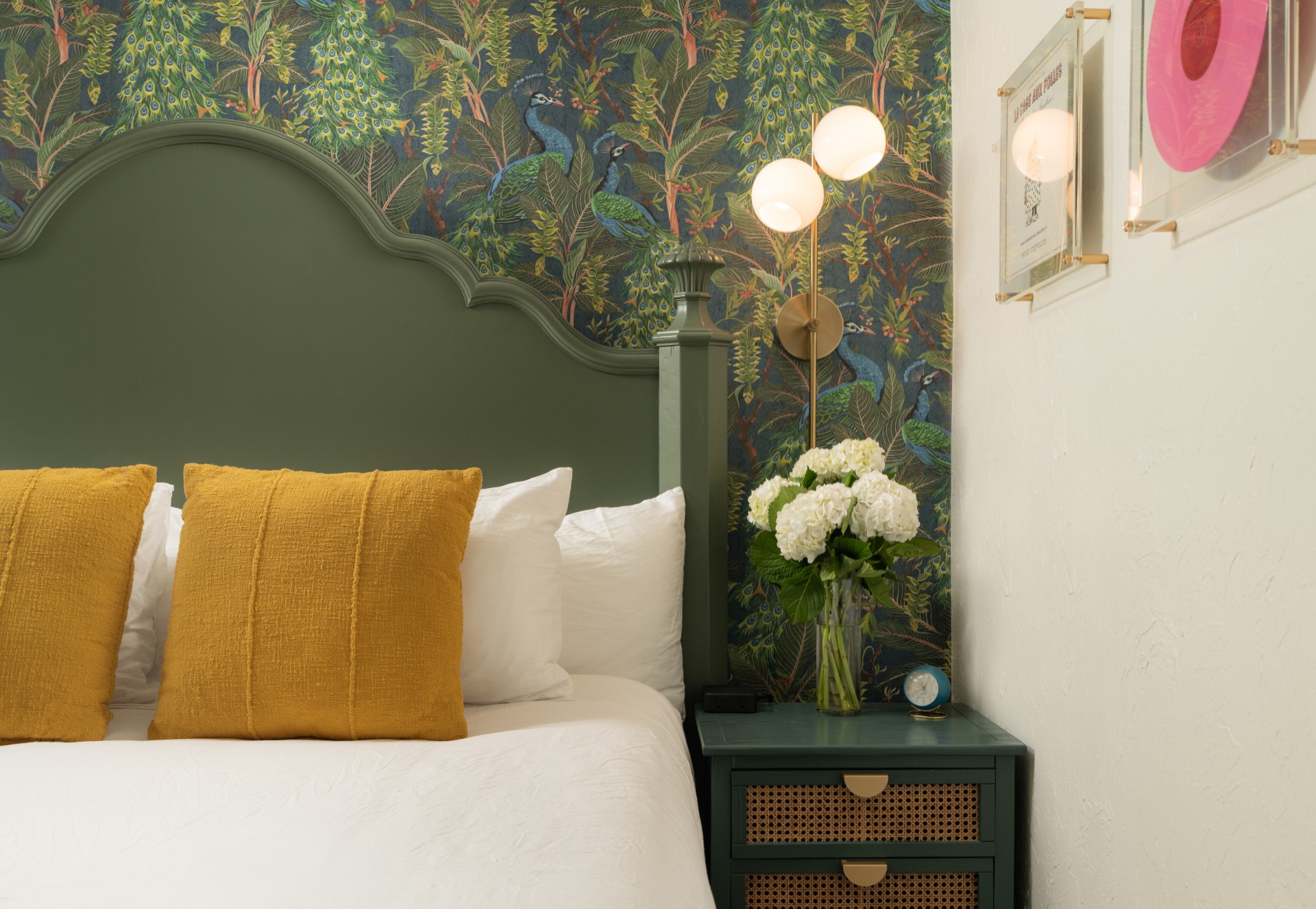 A close-up of a bed with a green headboard, yellow pillows, and white bedding, with a nightstand and lamp beside it.