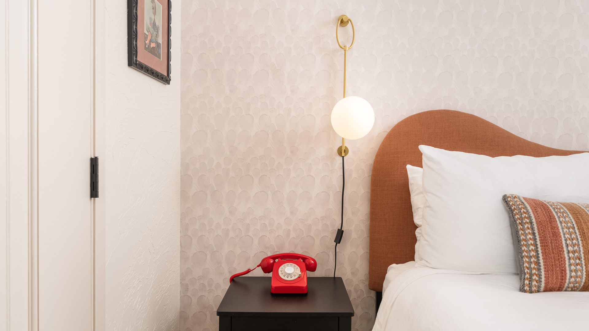 A close-up of a bed with a brown headboard, white bedding, and a red phone on a nightstand.
