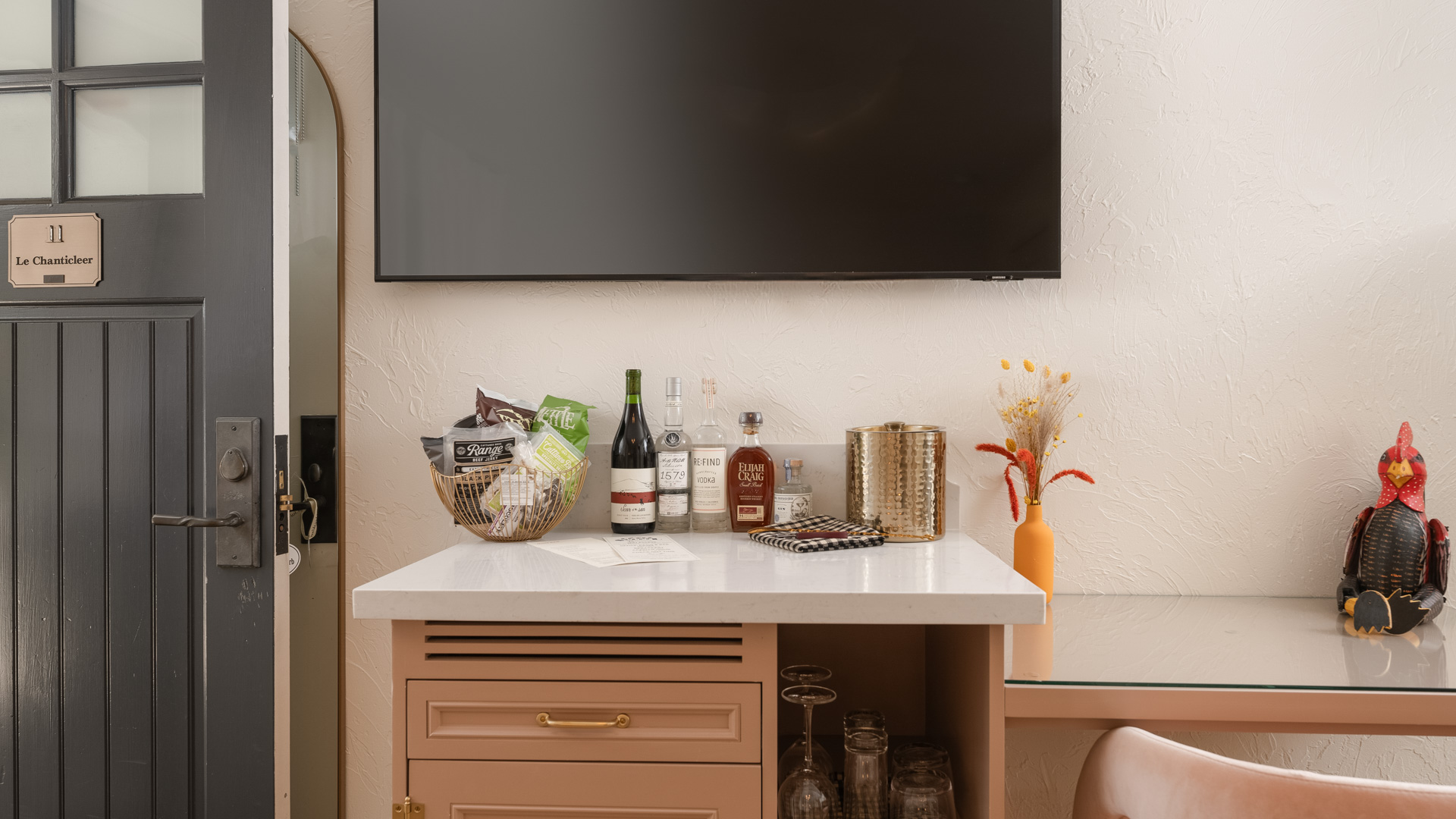 A well-stocked bar with wine, liquor, and snacks underneath a mounted TV