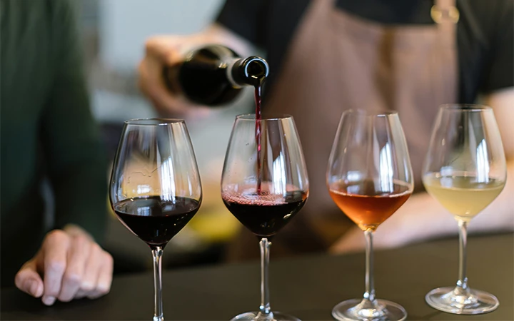 Four wine glasses on a table with wine being poured into one of them.