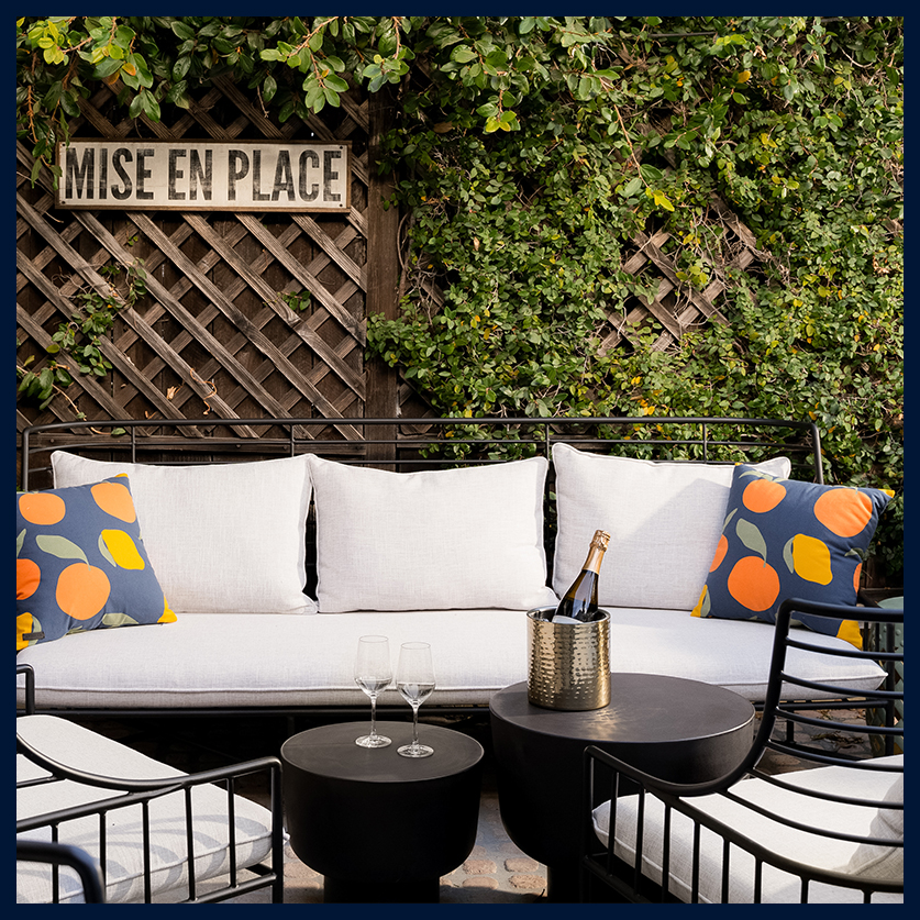 a white couch with orange pillows and a bottle of wine on a table