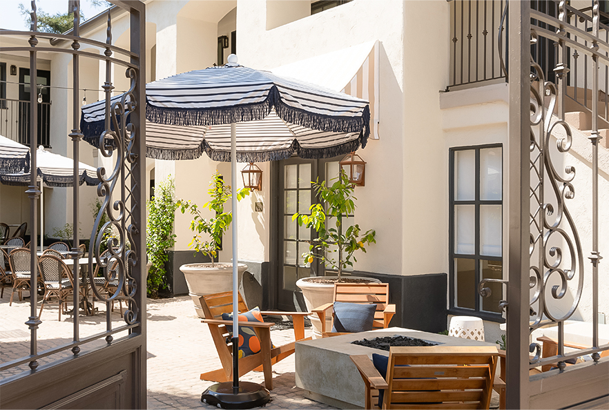 A cozy outdoor seating area with a fire pit, umbrella, and wrought iron gate.