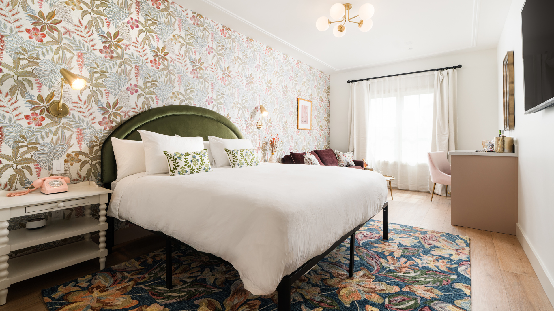 A wide view of a hotel room with a large bed, floral wallpaper, and a pink phone on a nightstand.