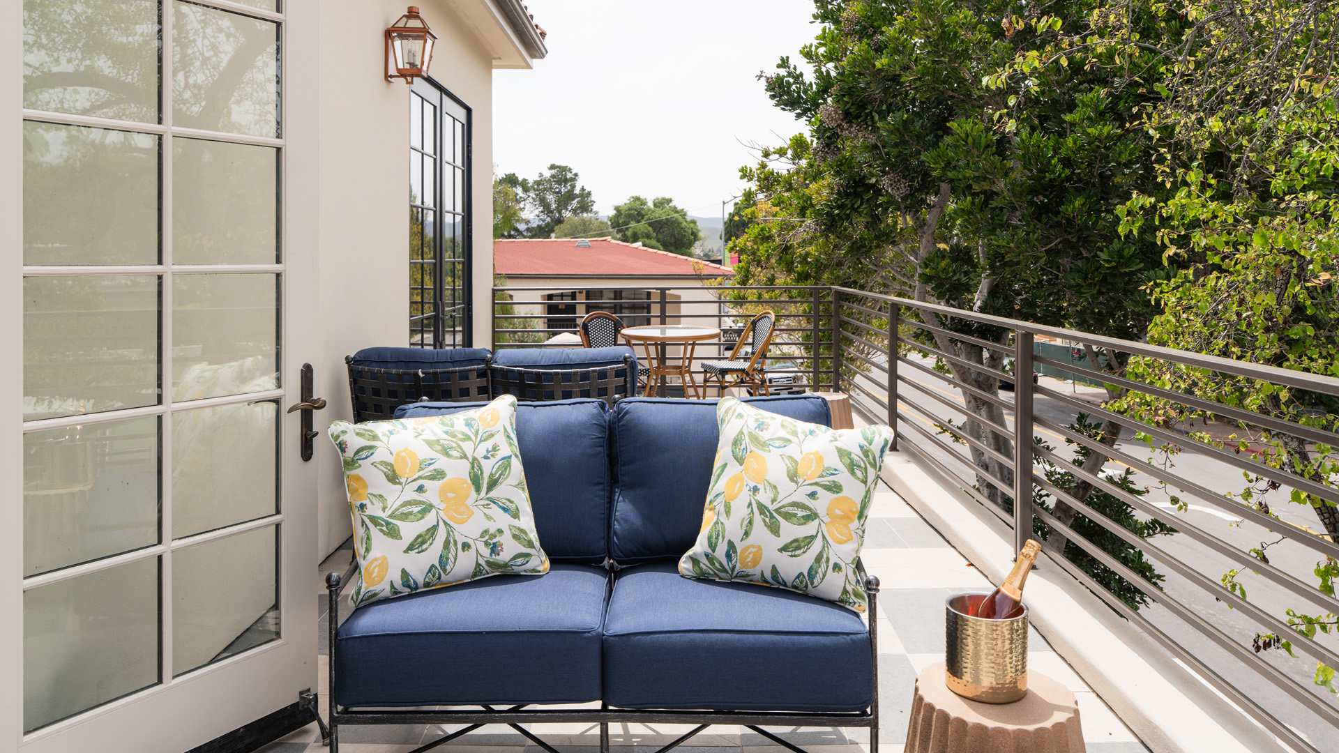 A blue couch with pillows on a balcony with a railing and trees in the background.