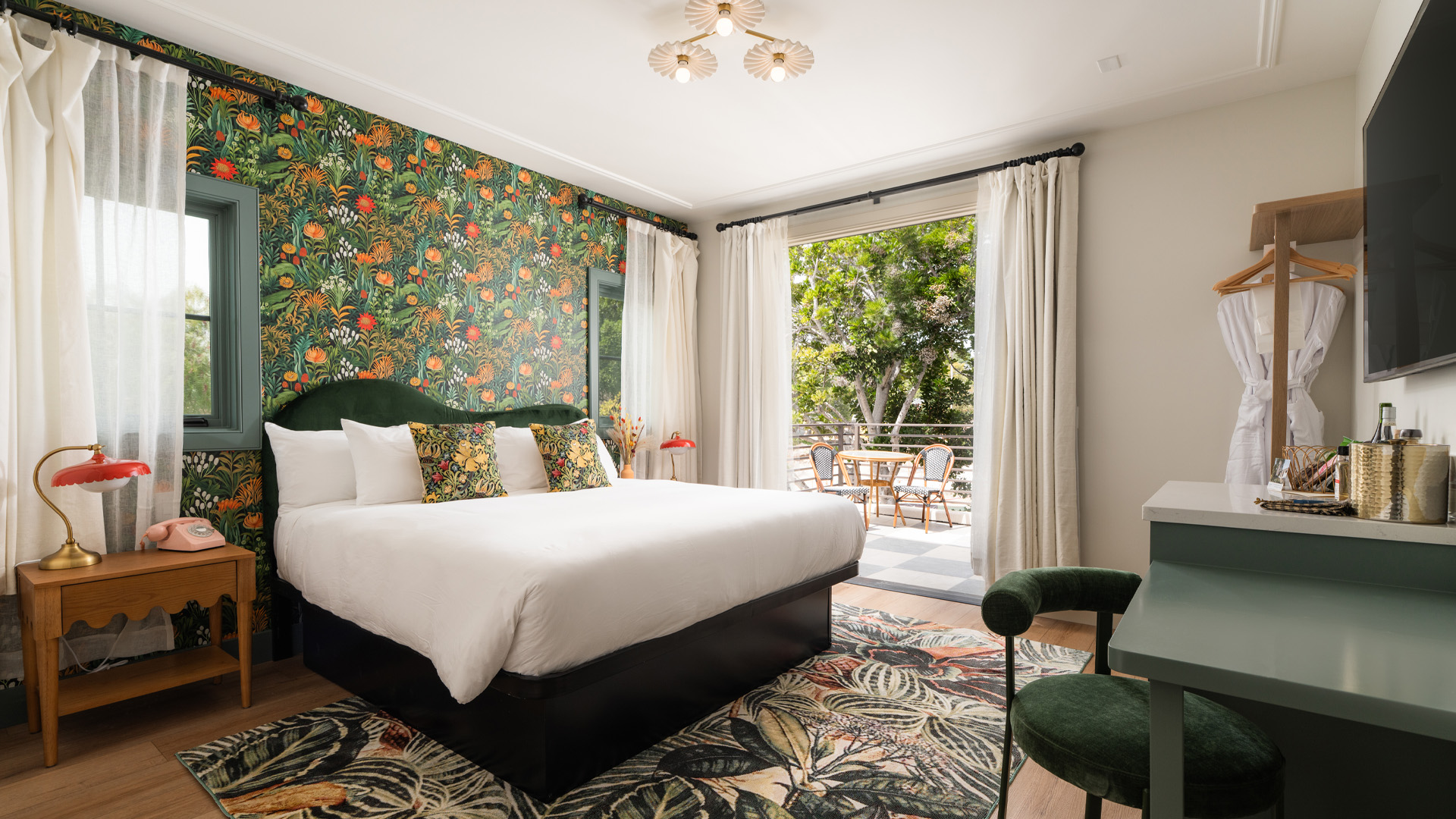 A wide view of a hotel room with a bed, desk, chair, and sliding door leading to a balcony.