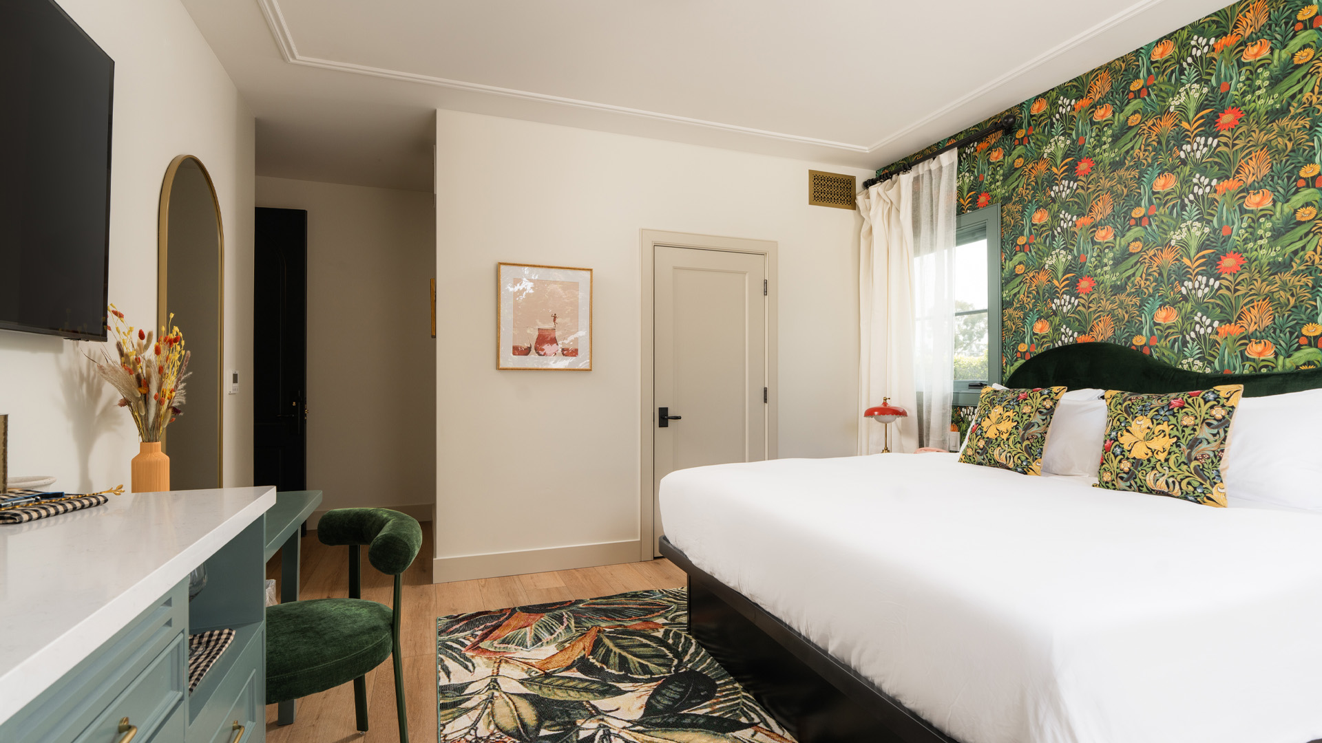 A wide view of a hotel room with a bed, desk, TV, and mirror