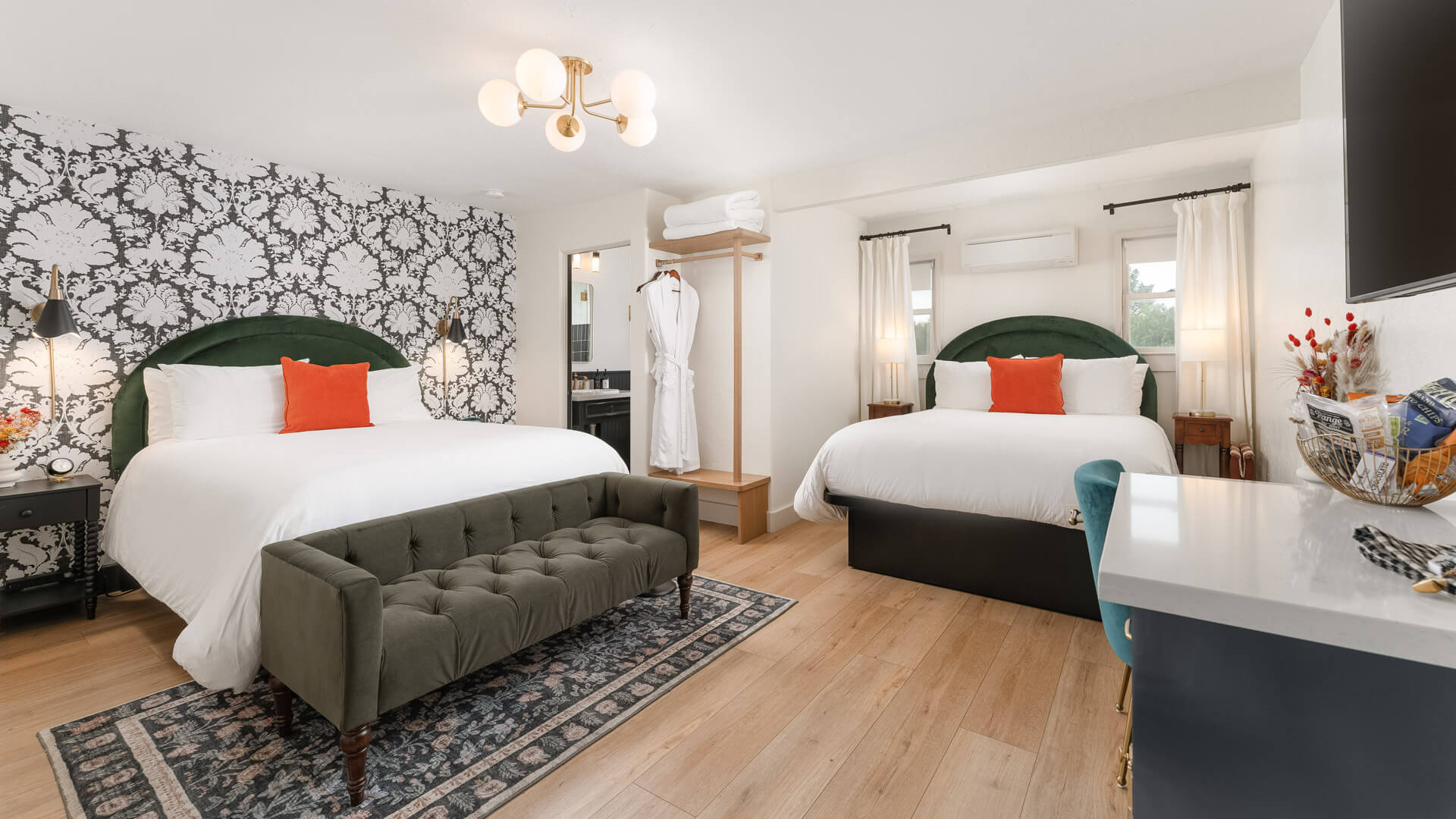 A wide view of a hotel room with two beds, a gray sofa, and a floral wallpaper.