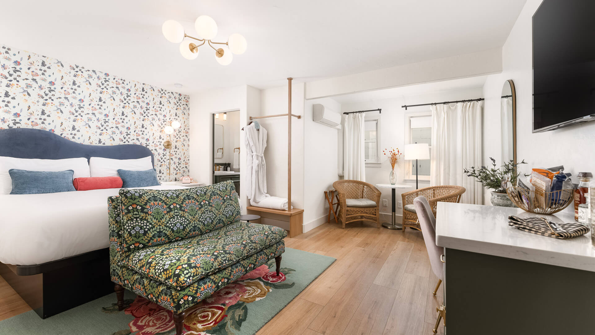 A wide view of a hotel room with a bed, chair, desk, and TV.