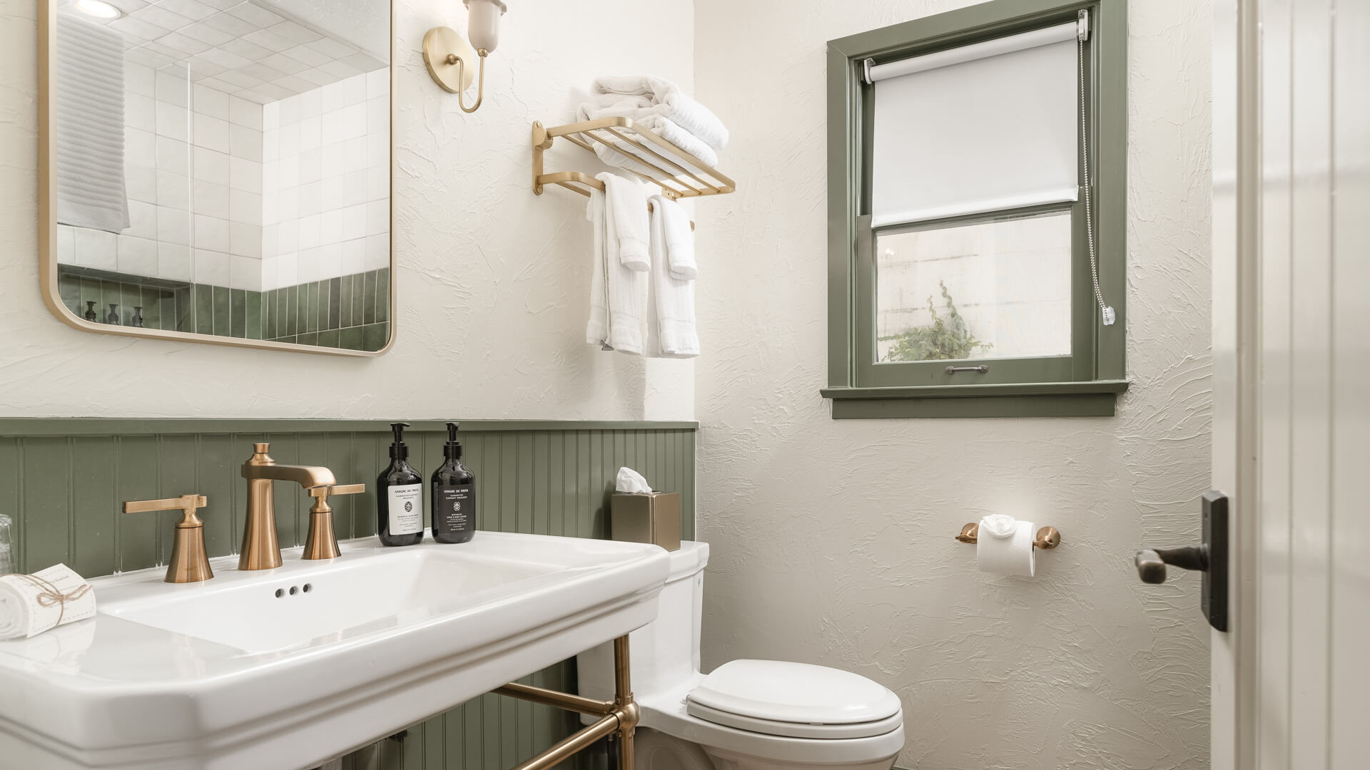 A clean and stylish bathroom with a white sink, gold faucet, and green wainscoting.
