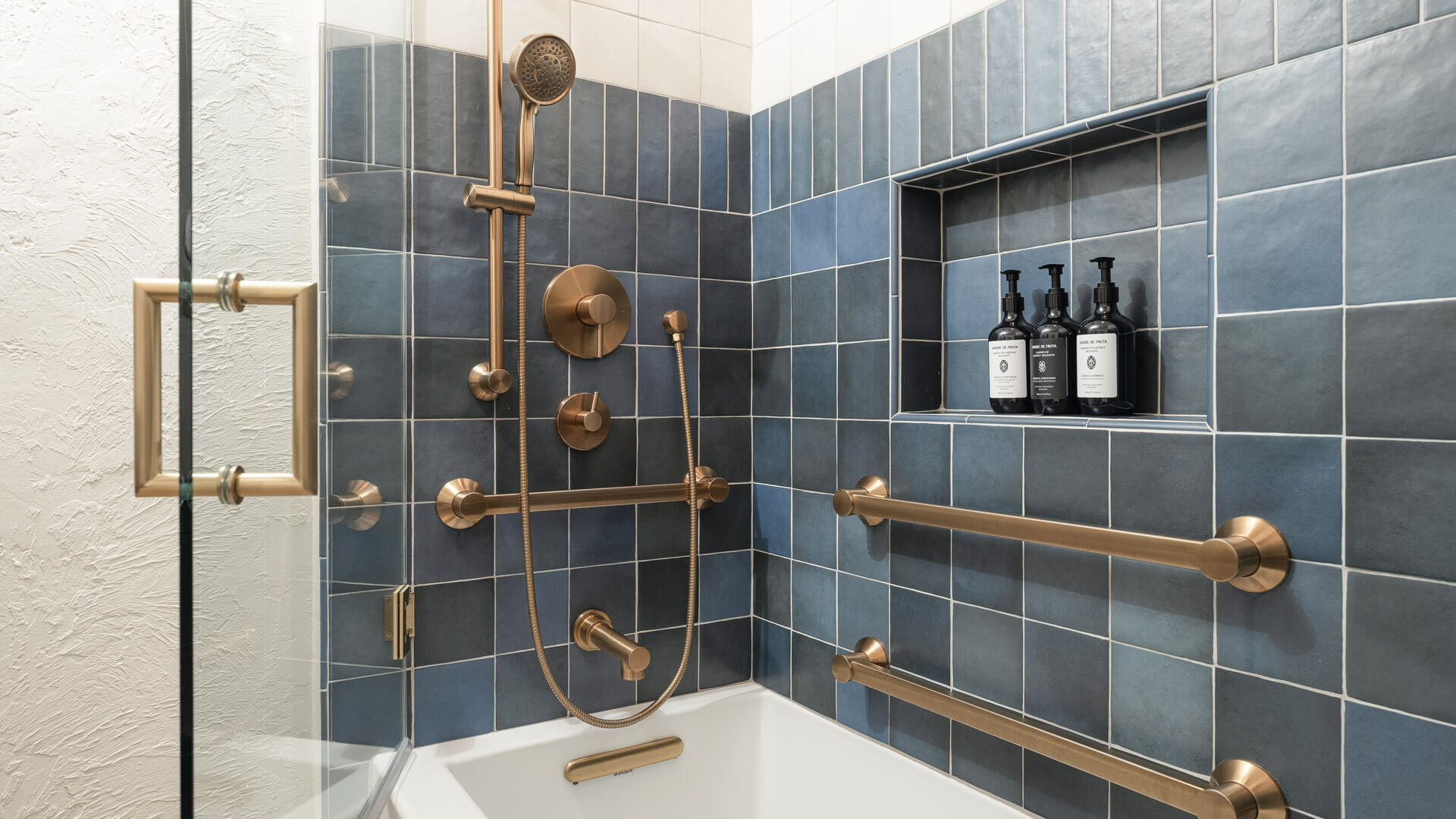 A bathroom shower with blue tiles, gold fixtures, and a bathtub.