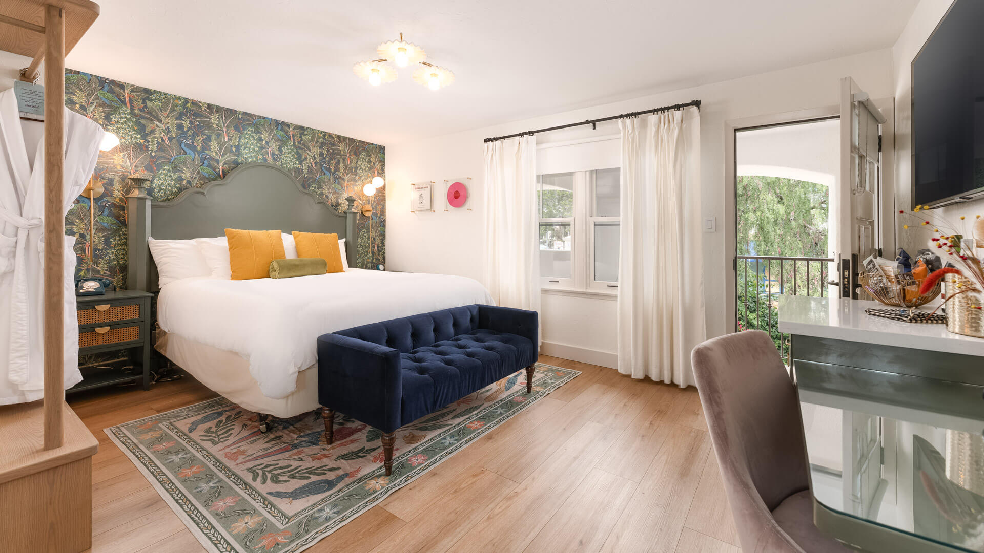 A wide view of a guest room with a large bed, desk, chair, and balcony door.