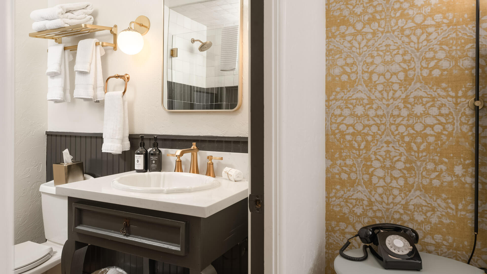 A bathroom sink area with a white sink, gold faucet, and dark cabinet.