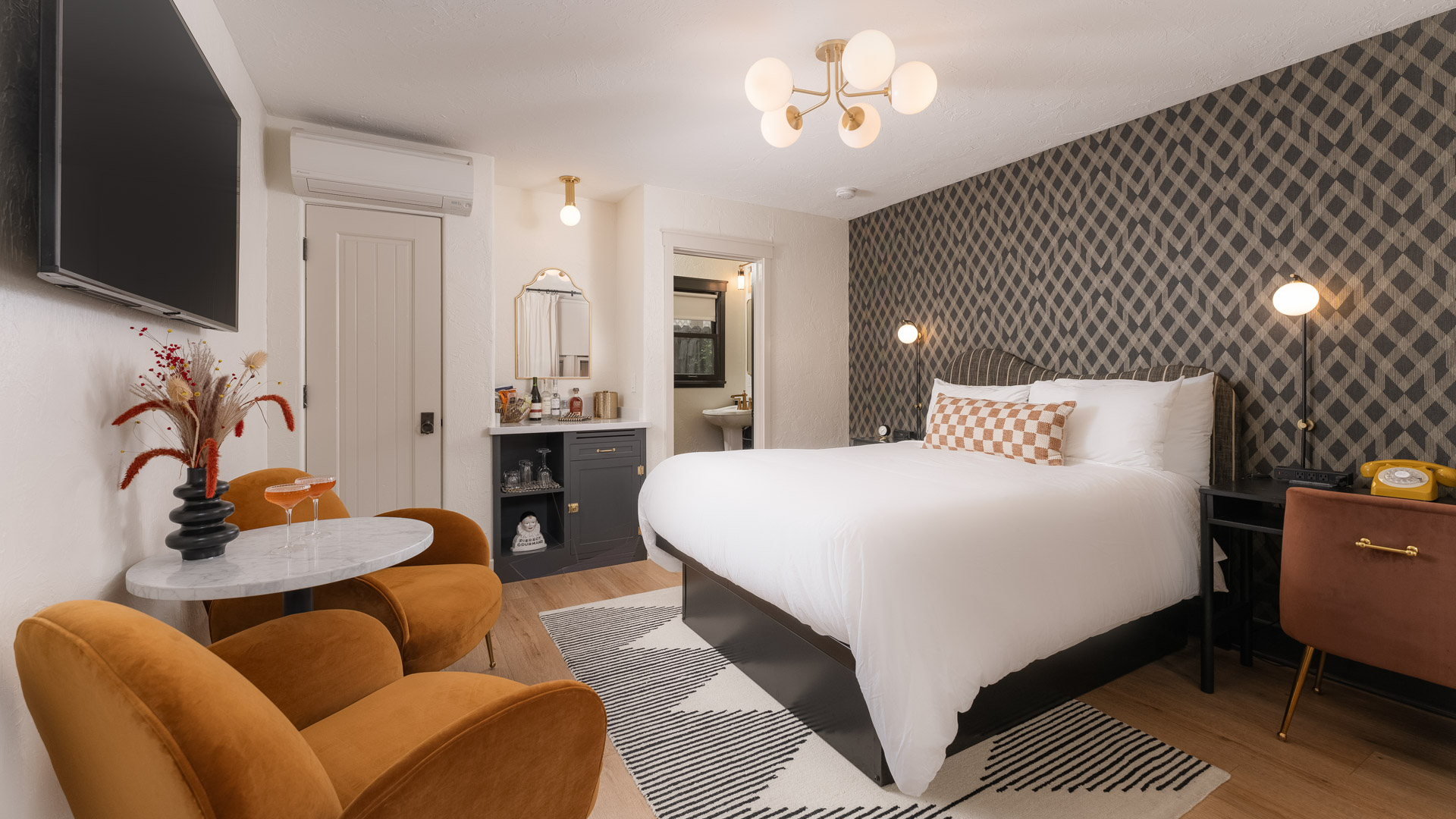 A hotel room with a bed, TV, table, chairs, and carpet.