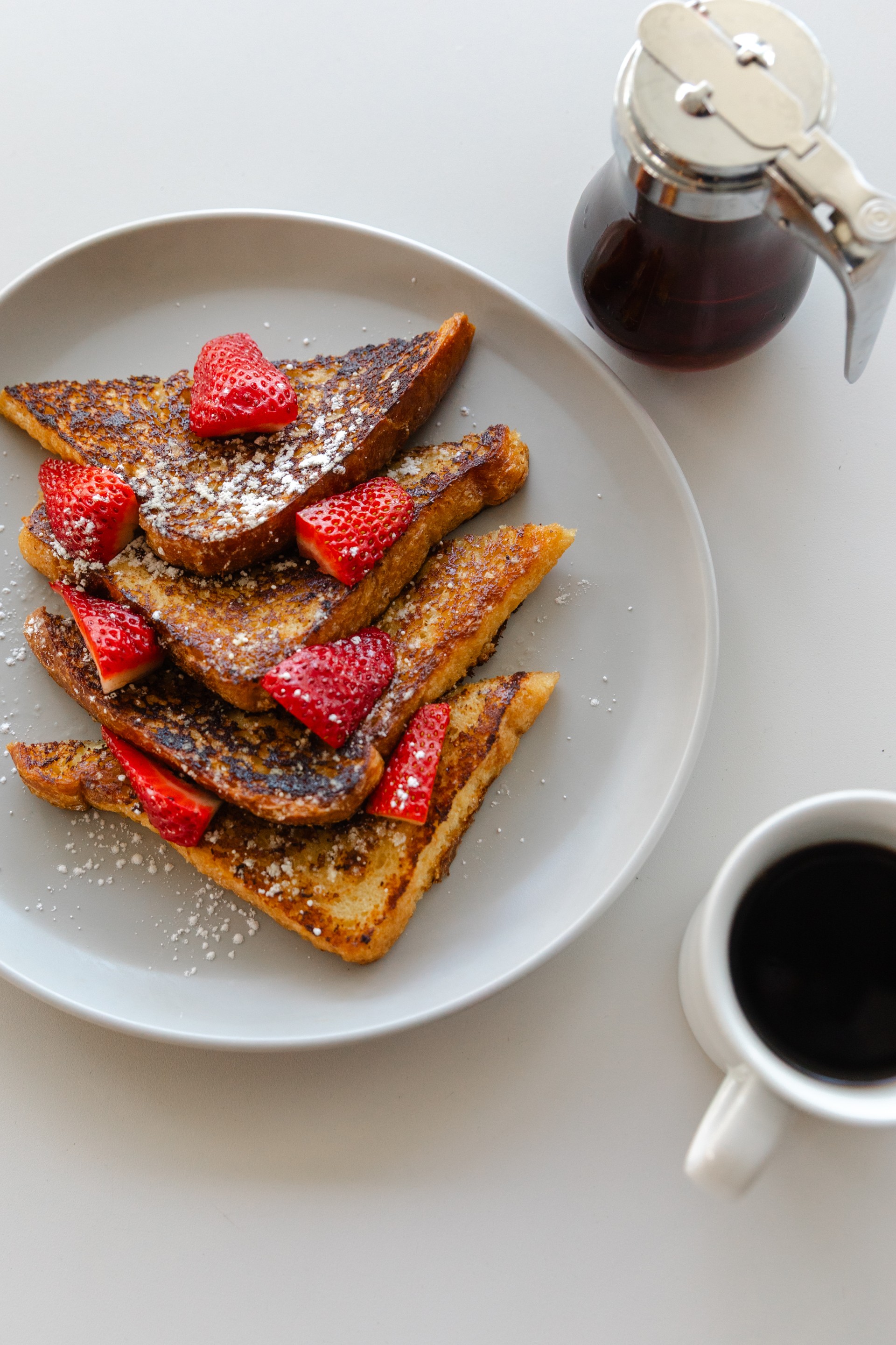 a plate of french toast with strawberries and a cup of coffee