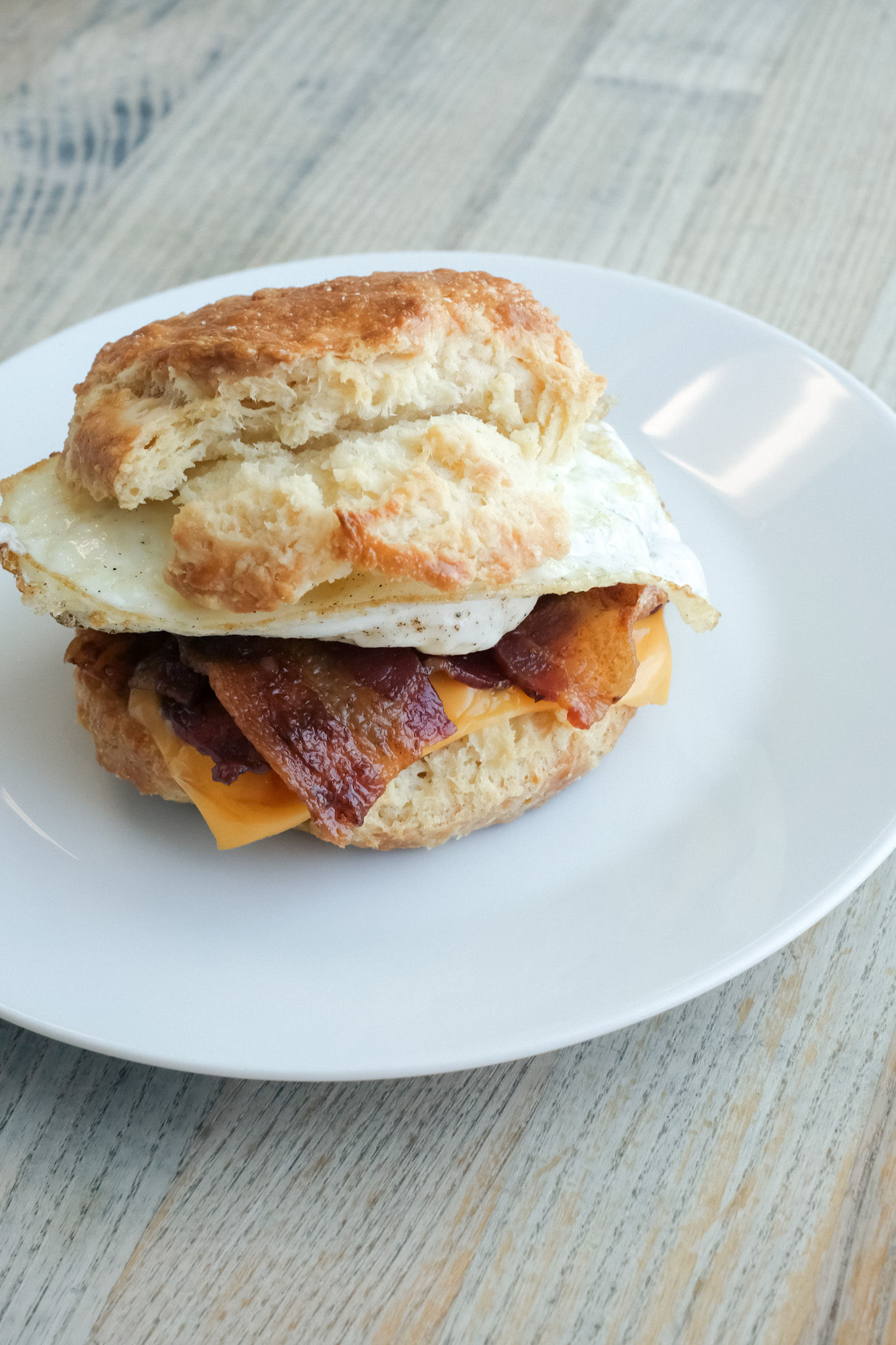 a biscuit sandwich with egg and bacon on a white plate