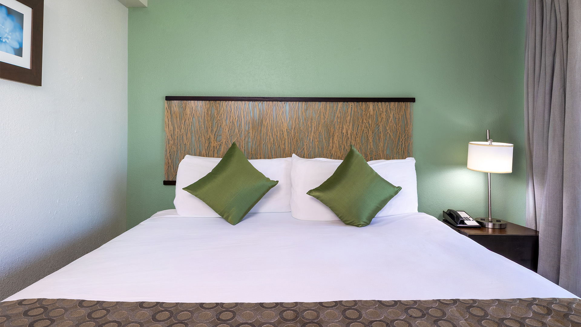 A neatly made hotel room with a large bed, wooden headboard, and green accent pillows.