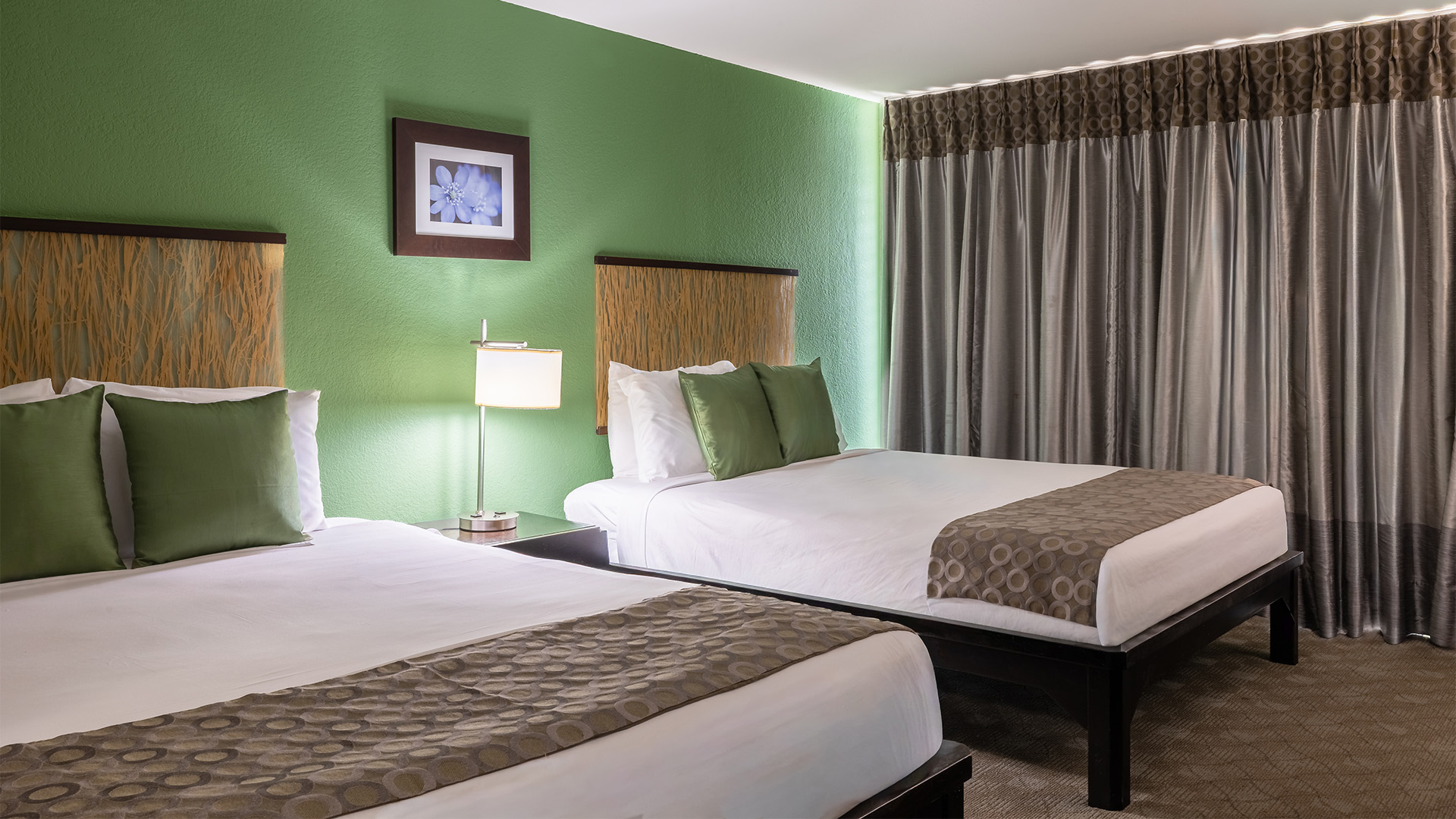 A hotel room with two twin beds, green walls, and brown curtains.