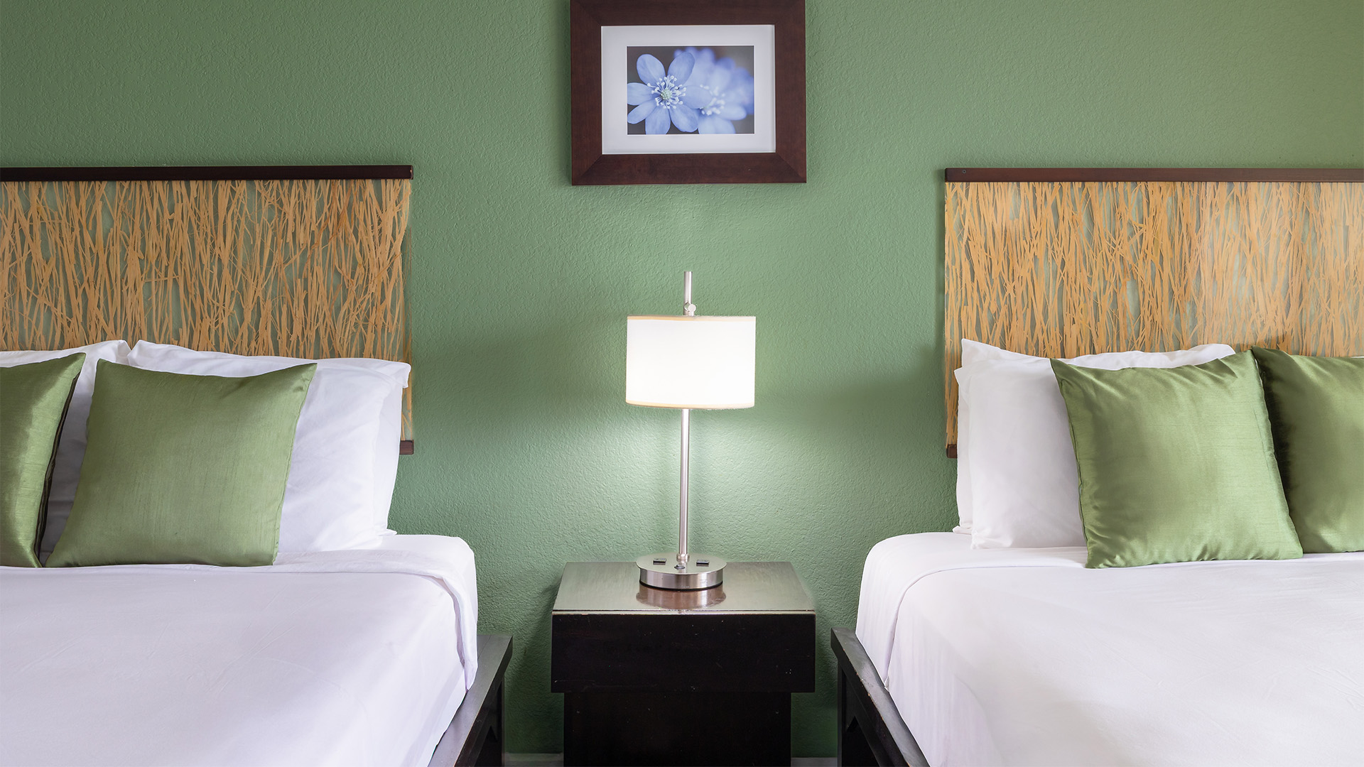 A hotel room with two twin beds, green walls, and wood headboards.