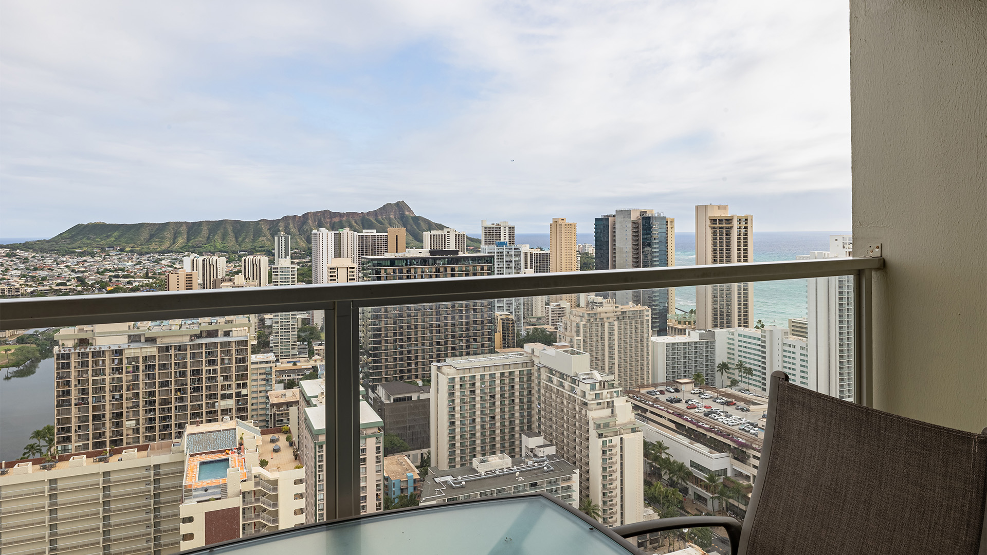 A balcony with a glass railing and a chair overlooking a cityscape with a mountain in the distance.