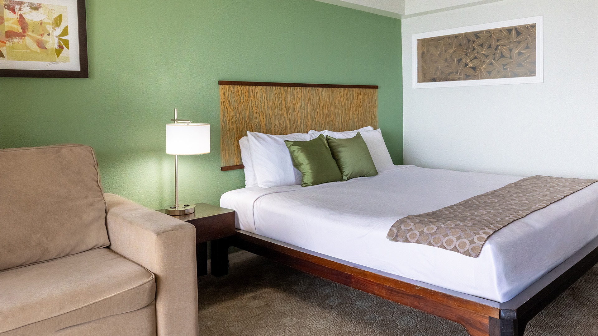 A hotel room with a bed, chair, lamp, and artwork on the walls.
