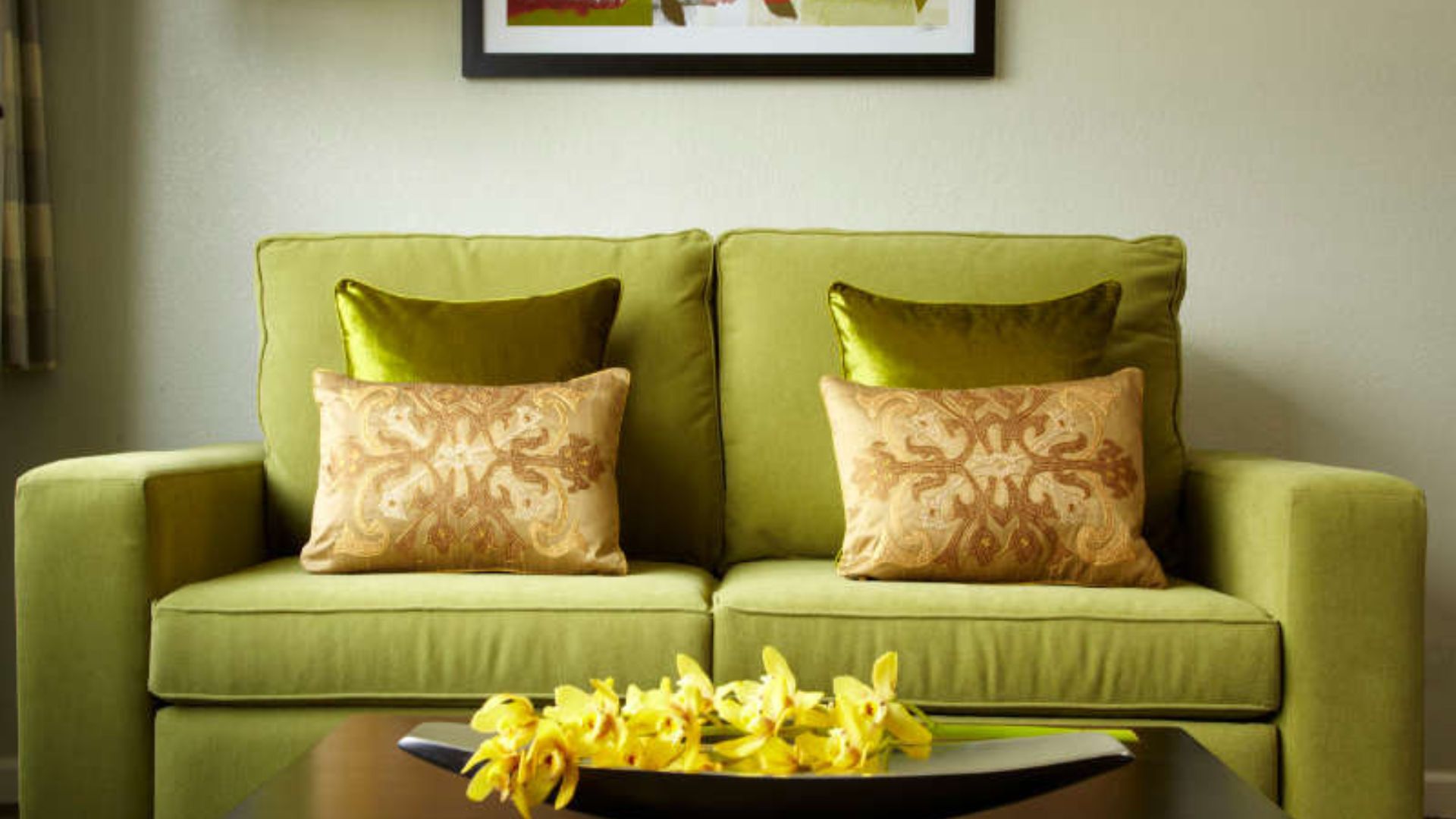 A green couch with throw pillows and a coffee table with yellow flowers in a lobby area.