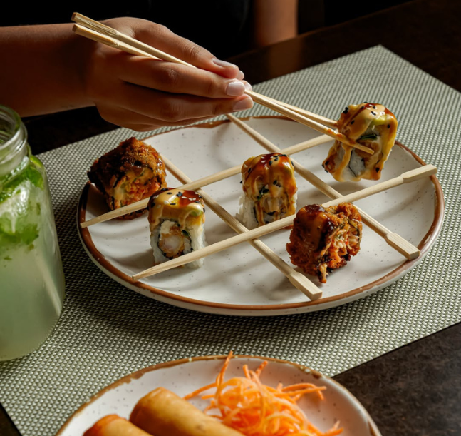 a hand holding chopsticks over sushi