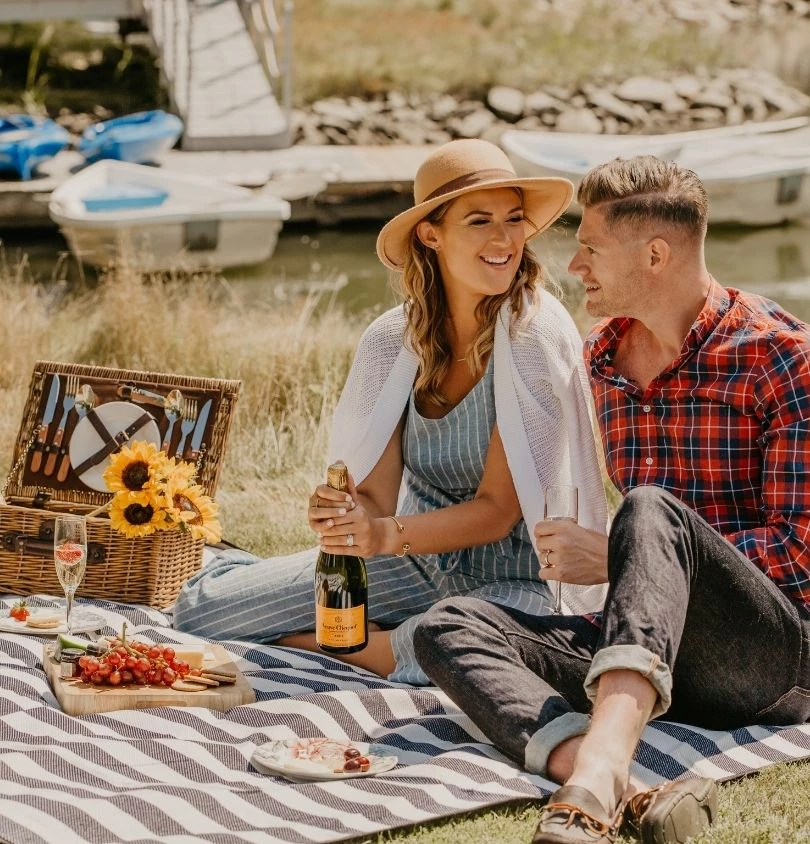 a man and woman sitting on a blanket with a picnic basket and wine