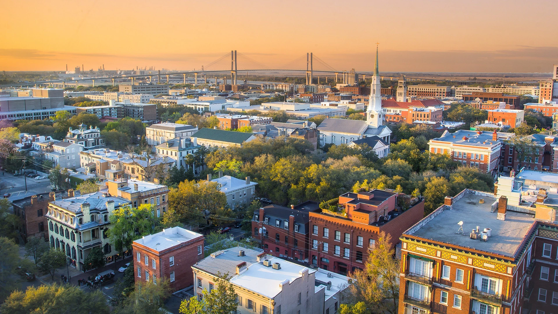 An aerial view of a city at sunset, with a bridge in the background.