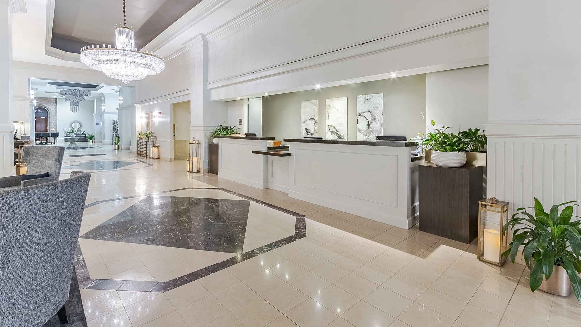 A bright and spacious hotel lobby with a reception desk, chandelier, and seating area.