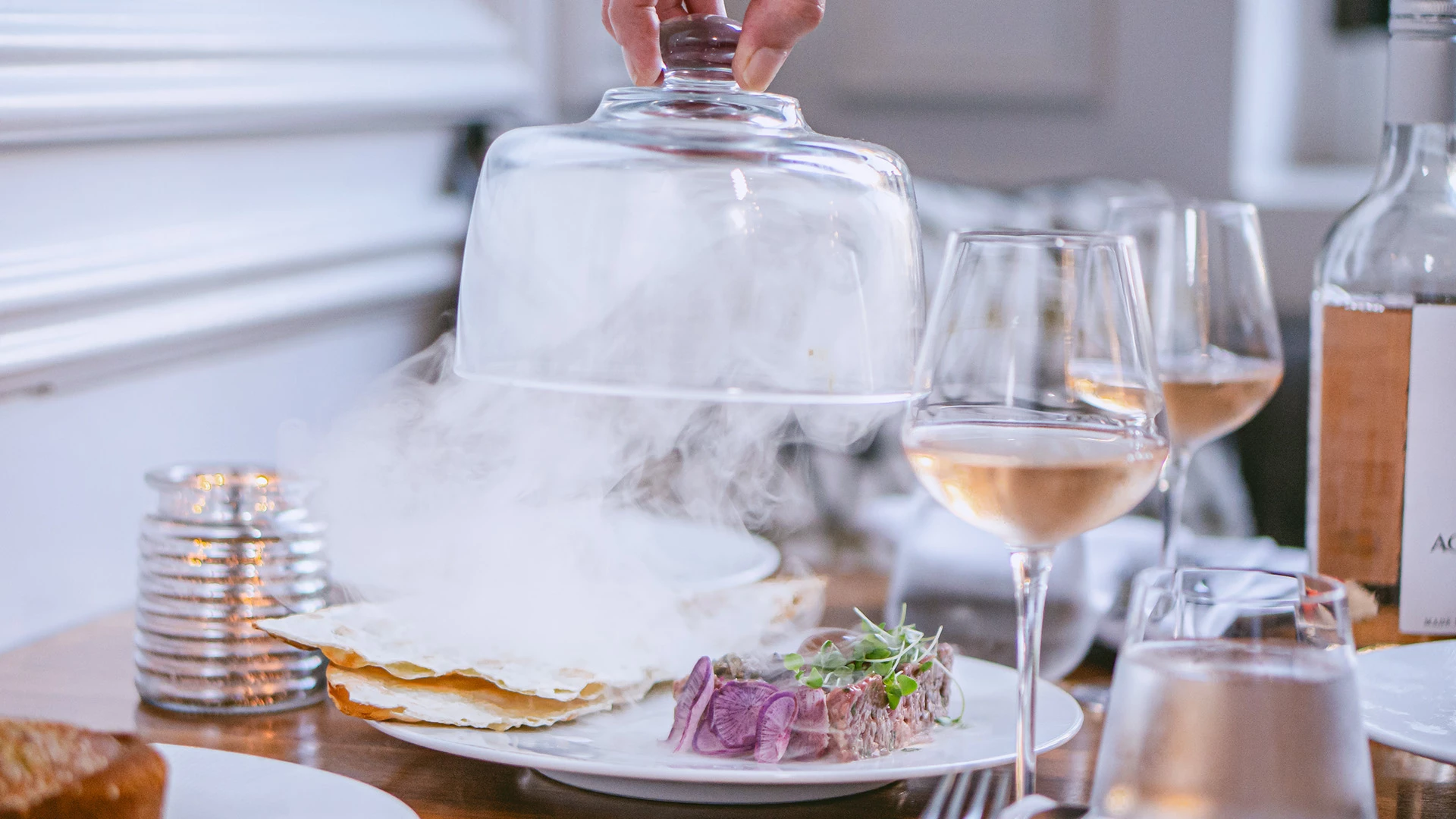 A table set with wine and a dish being served with steam rising.
