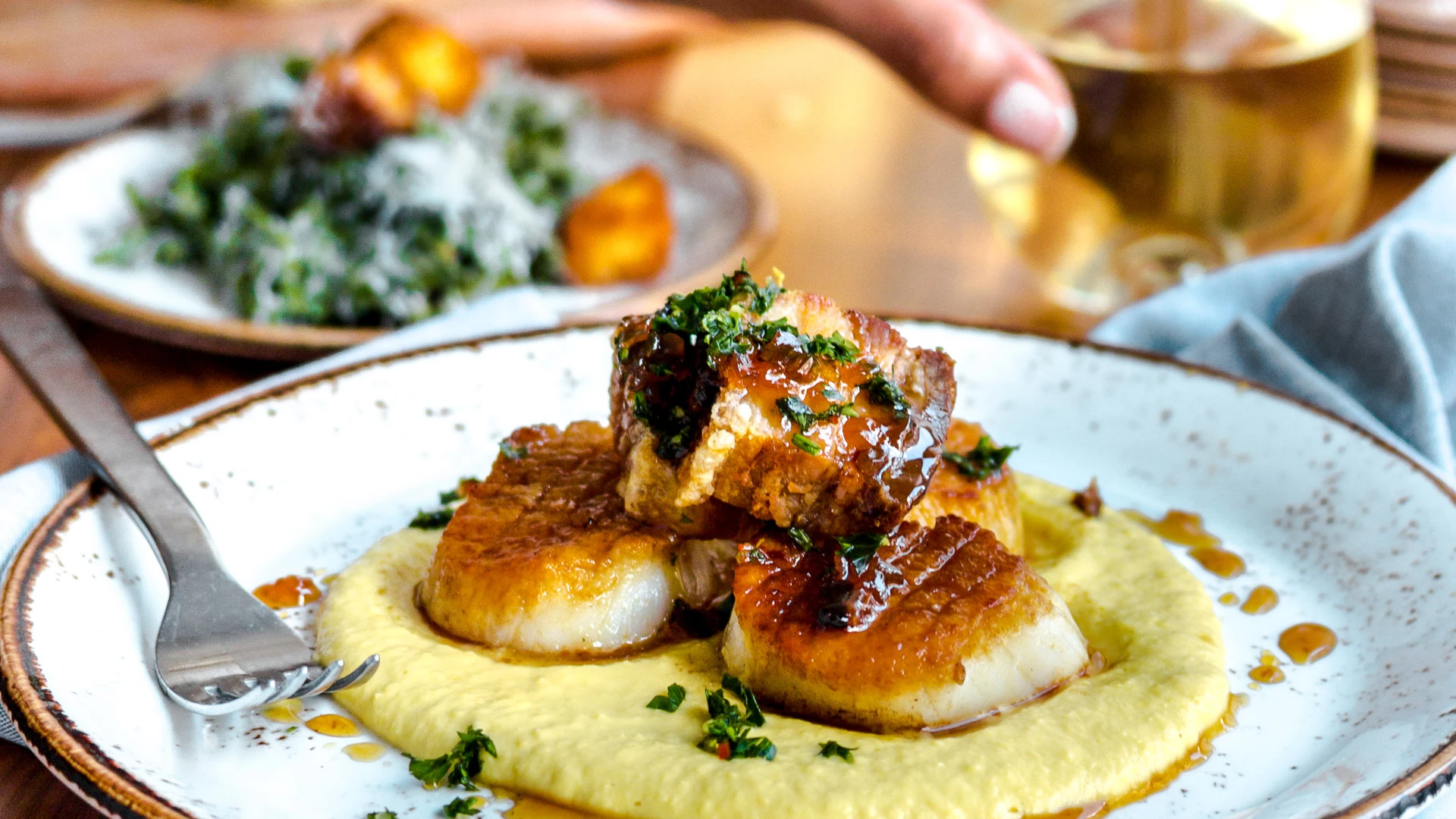 A plated dish of scallops on mashed potatoes with sauce and herbs.