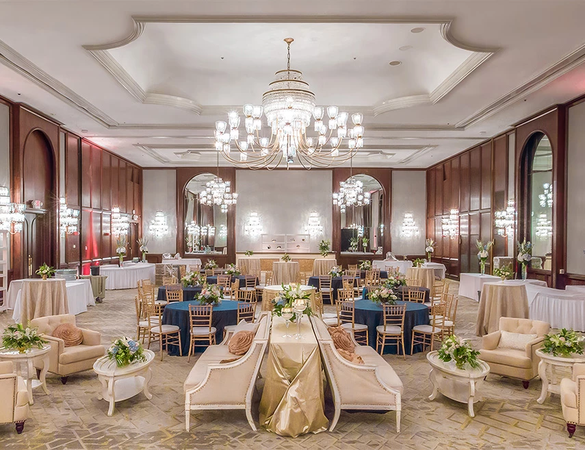 A large, elegantly decorated meeting room with tables, chairs, floral arrangements, and a chandelier.