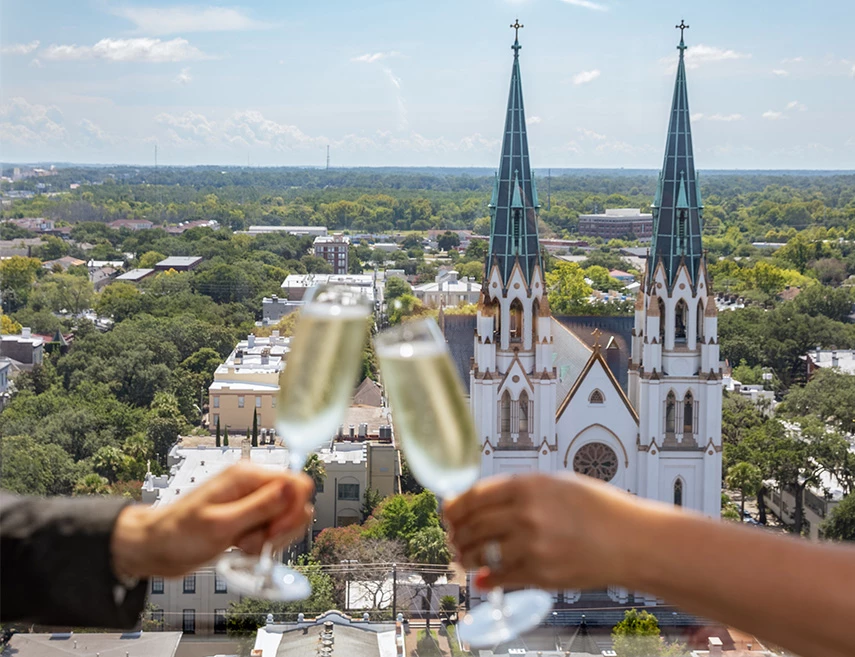 a city view with a church and two hands holding champagne glasses