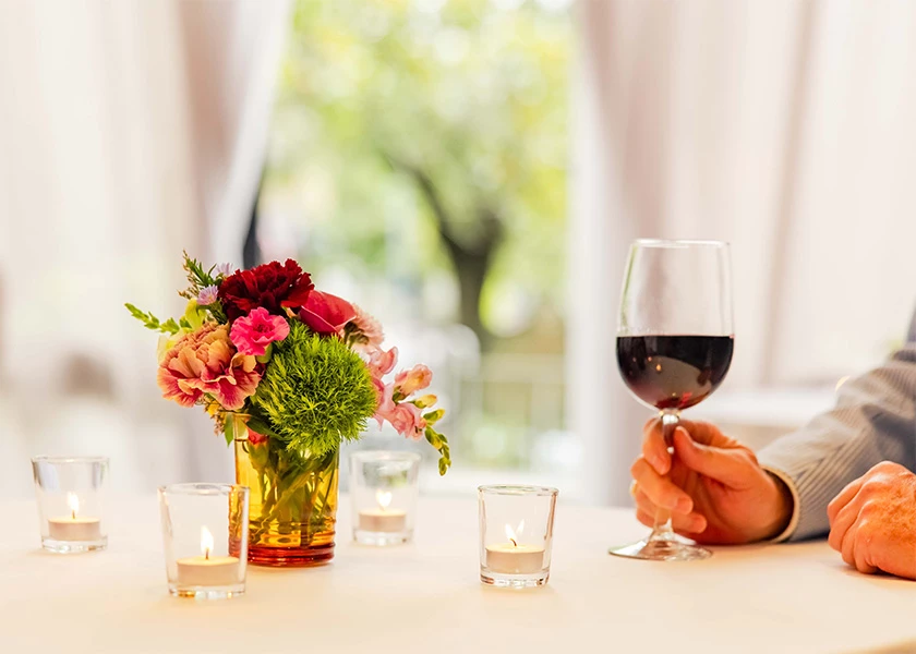 a table with a vase of flowers, wine glass, and candles
