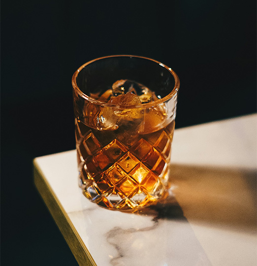 a glass of amber liquid with ice on a marble surface