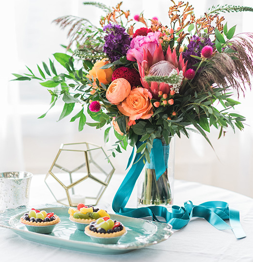 a bouquet of flowers in a vase next to a plate of fruit