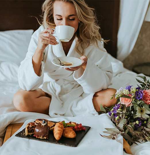 a woman in a white robe drinking tea and eating croissants