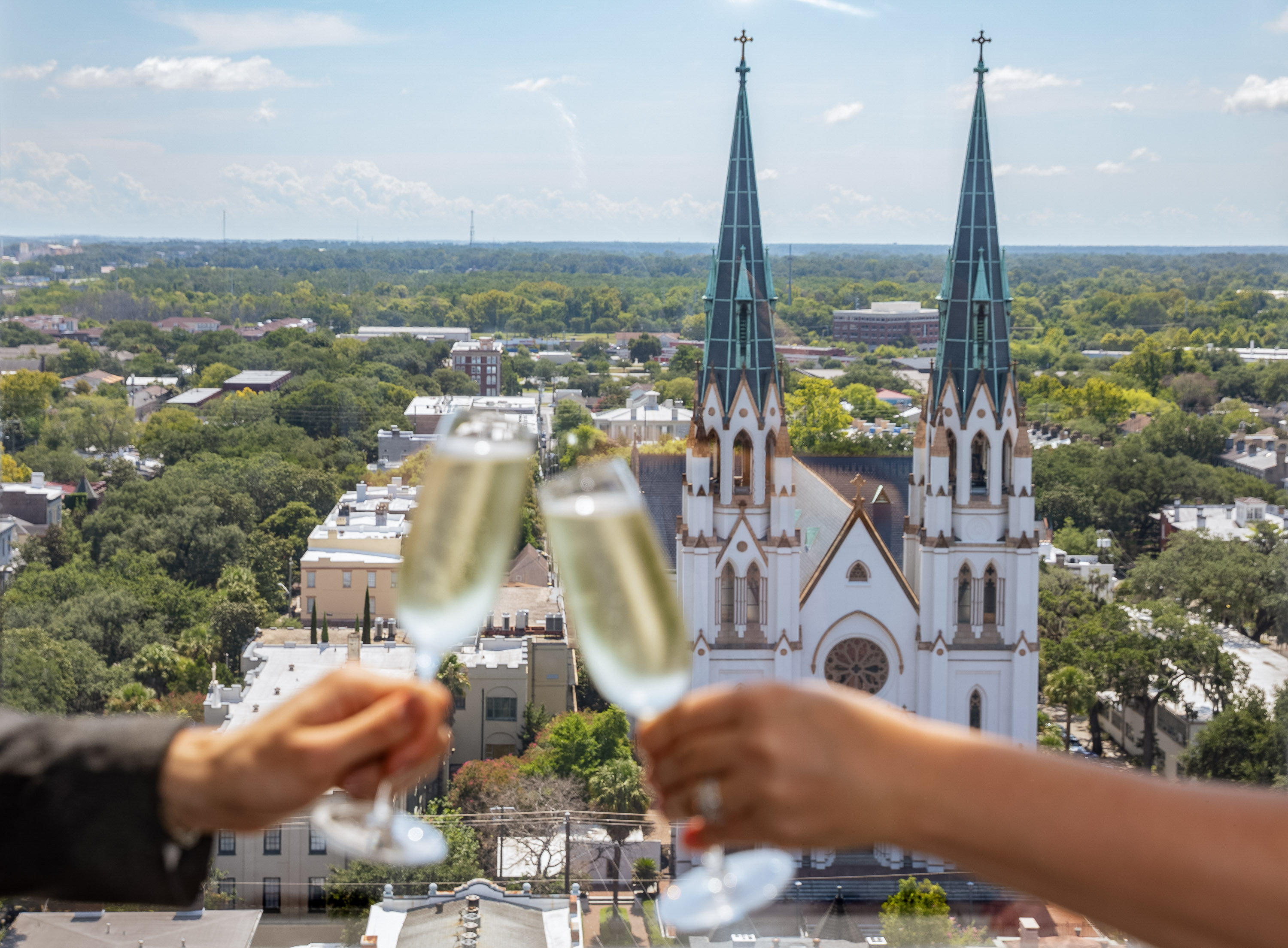 a couple of hands holding champagne glasses with a city in the background