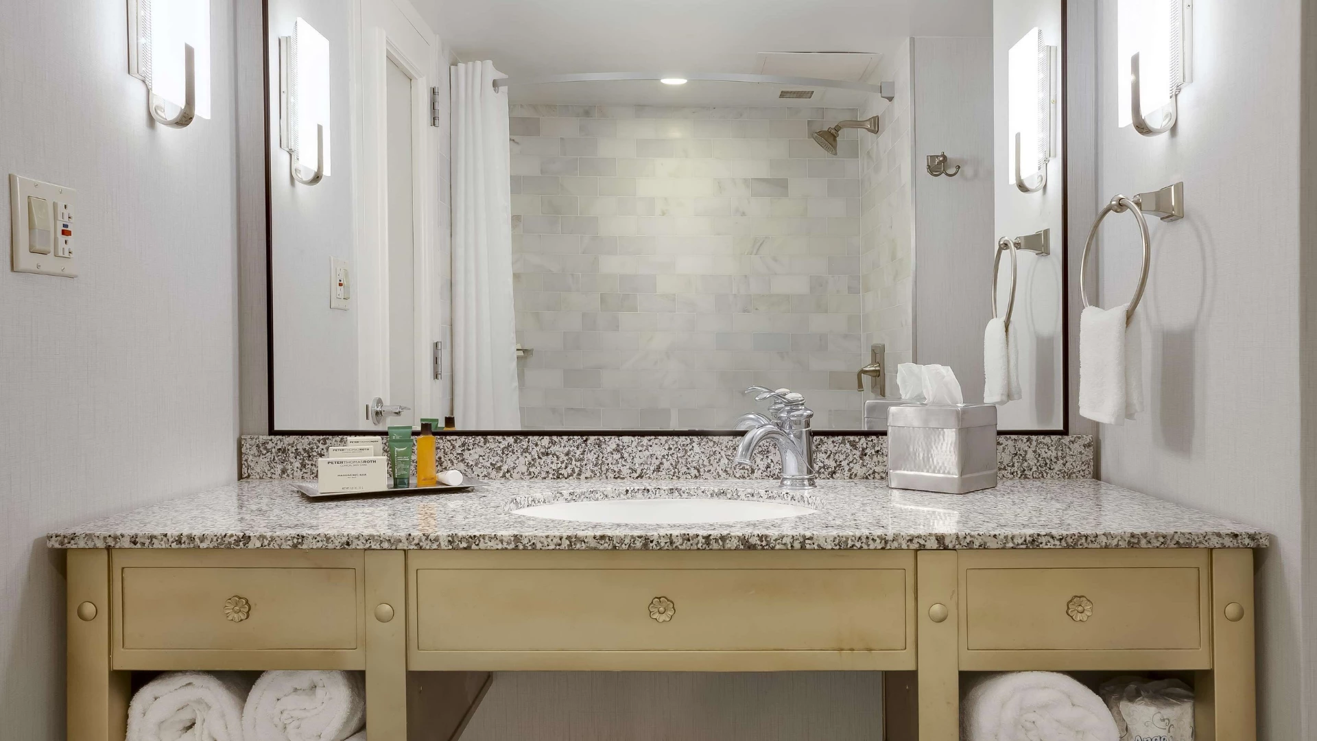 A clean and well-appointed bathroom vanity with a granite countertop, double sink, and large mirror.