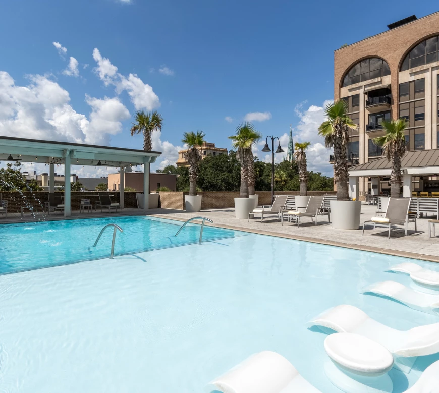 A swimming pool with lounge chairs and palm trees next to a building